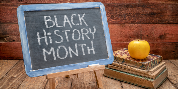 Black History Month written on a chalkboard, with a set of books and an apple next to the chalkboard