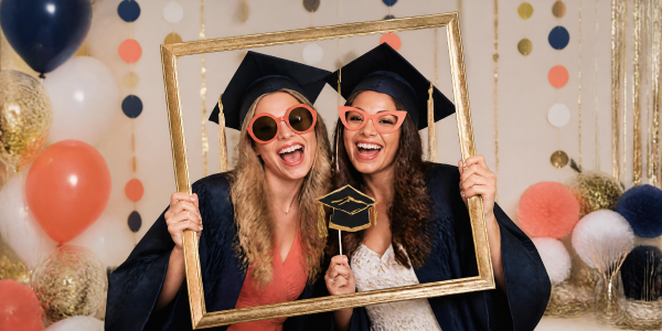 two female high school seniors having fun in a Photo Booth at a graduation party