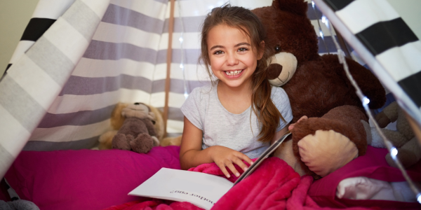 young elementary-aged girl reading a book inside a striped tent indoors